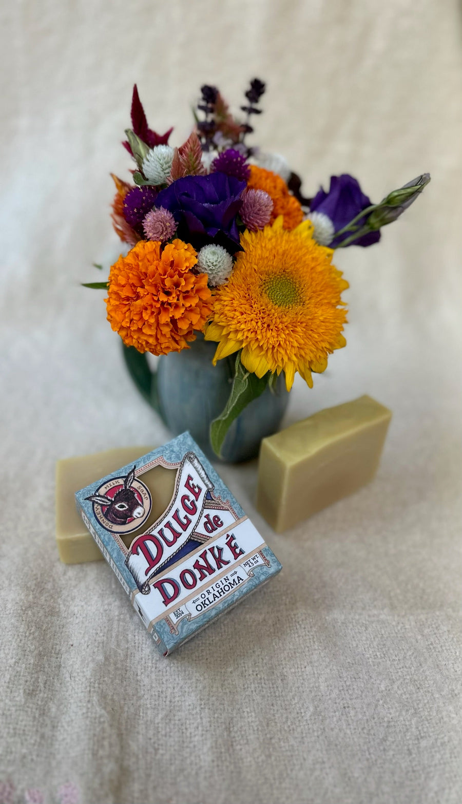Unscented soap, package, and colorful flowers arranged on a pale surface