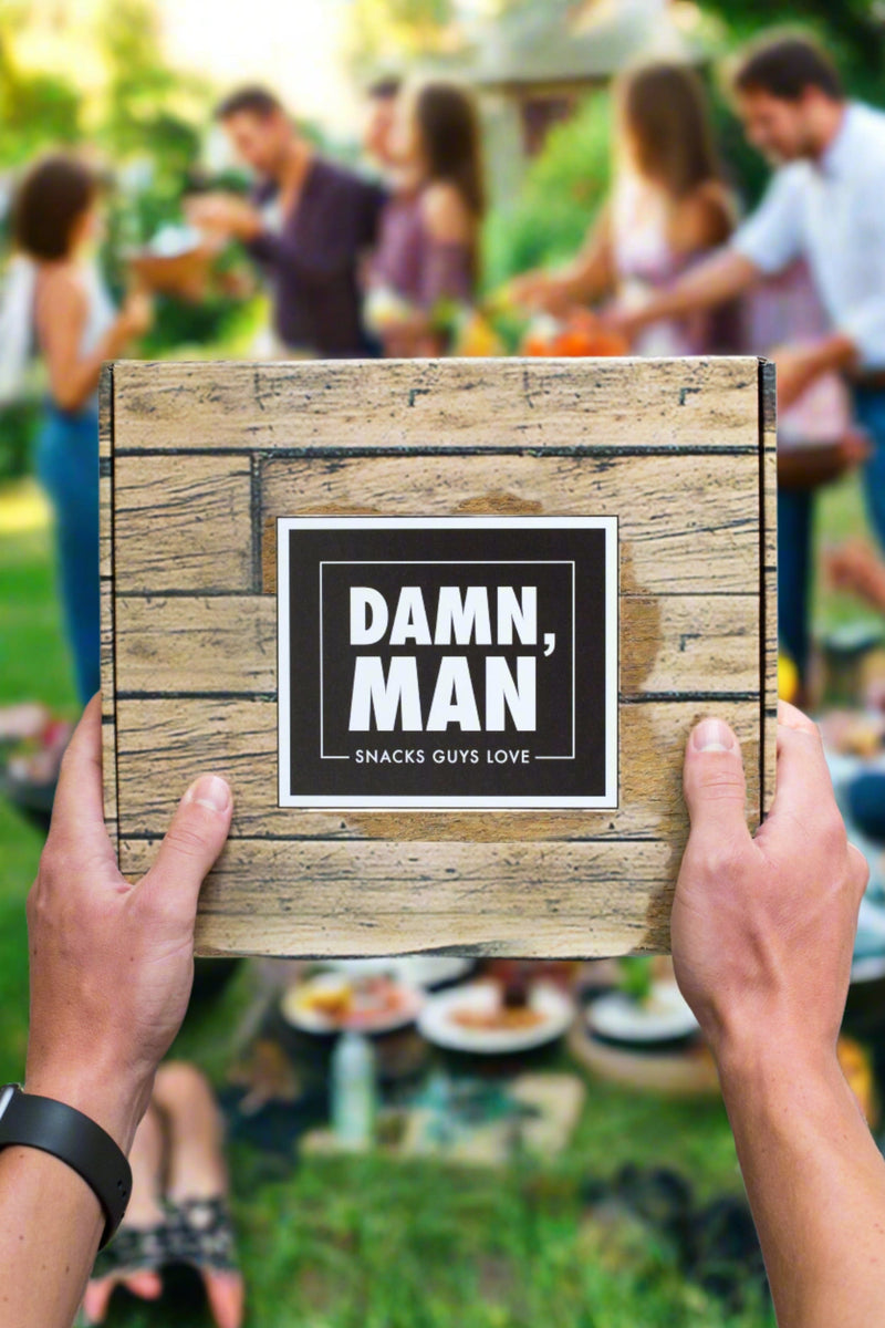 Man holding Manly Mixed Nuts Box at an outdoor barbecue with friends in the background