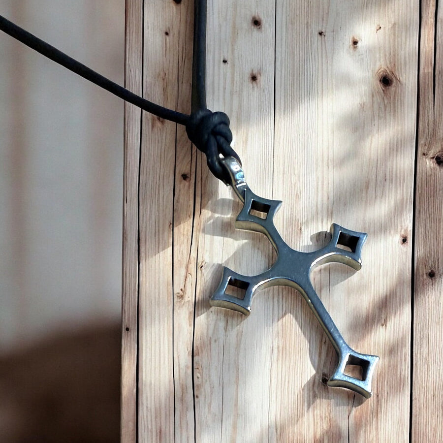 Gothic cross and black leather cord against weathered wood