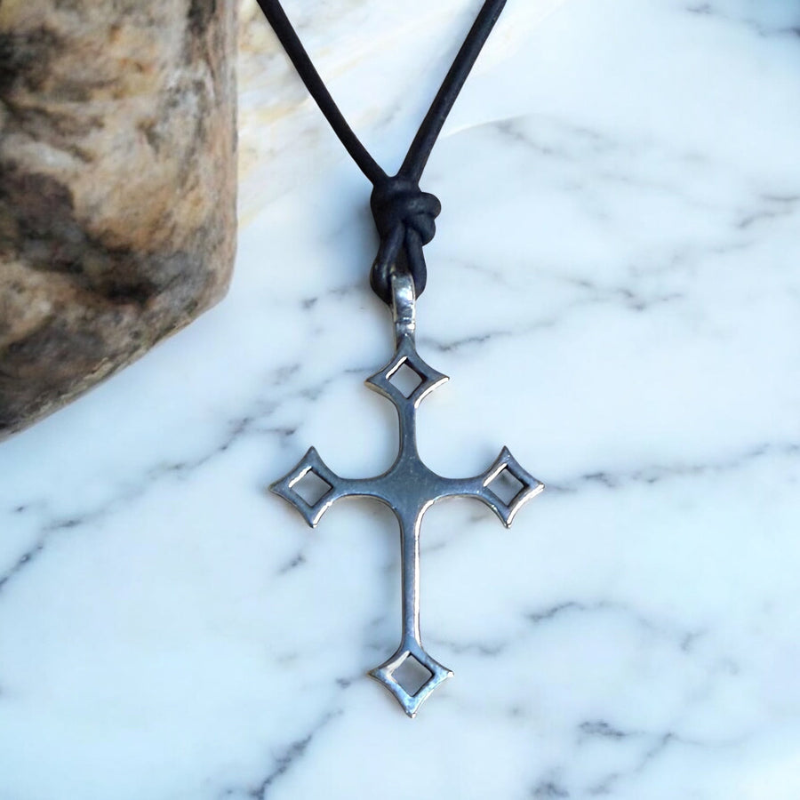 Gothic cross on black leather cord against pale stone