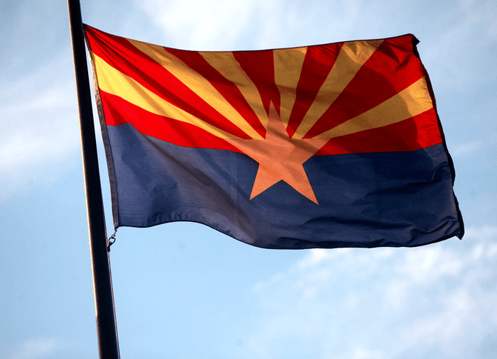 Arizona state flag flying outdoors from a flagpole against a blue sky