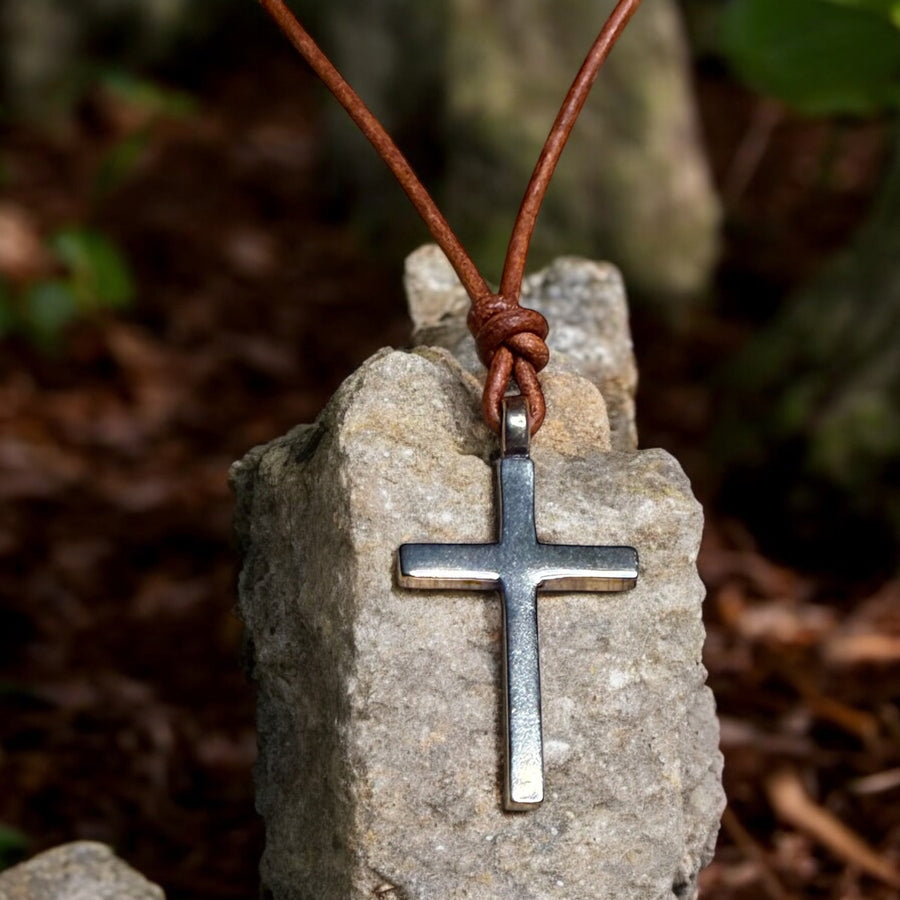 Classic cross on brown leather cord against rock