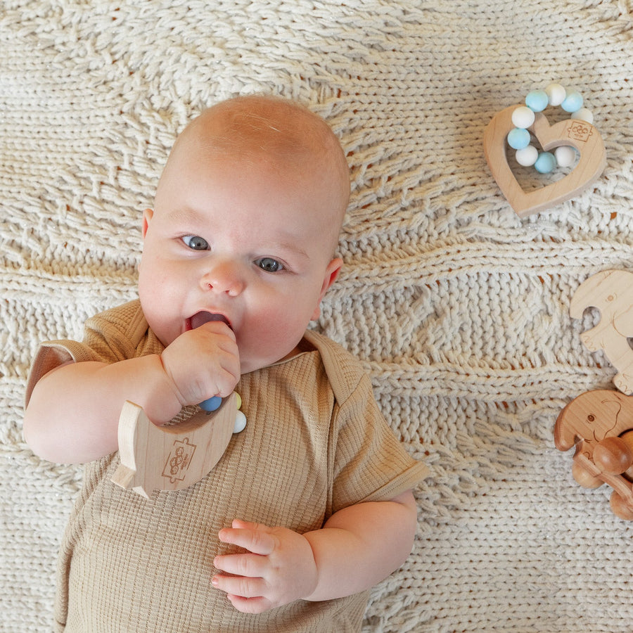 Baby holding a wooden teether with silicone beads during supervised play