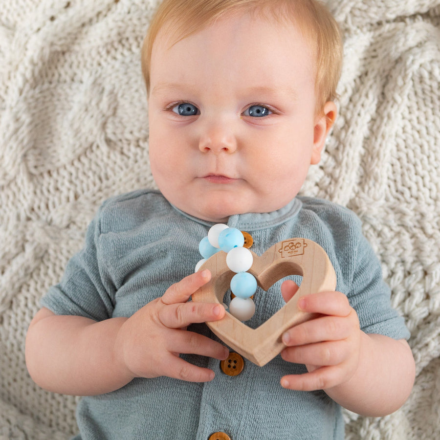 Baby holding a wooden teether with silicone beads during supervised play
