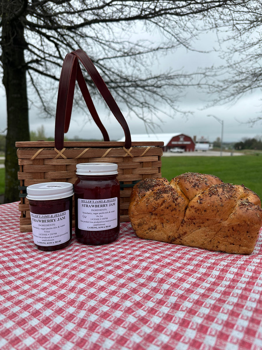 Two sizes of Miller’s Strawberry Jam beside bread and a picnic basket; jars sold separately.
