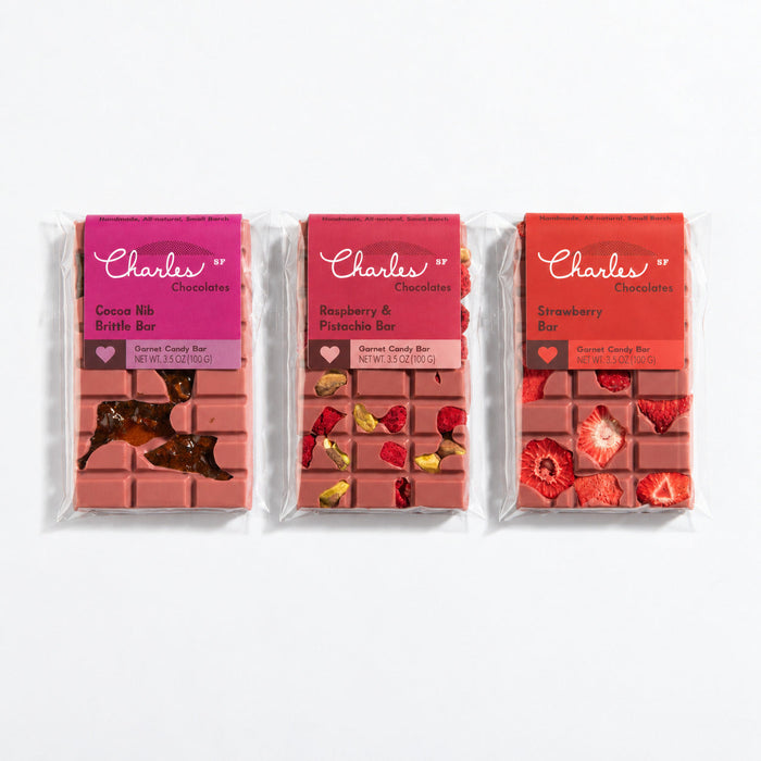 Three wrapped ruby chocolate bars in strawberry, raspberry-pistachio, and cocoa-nib flavors