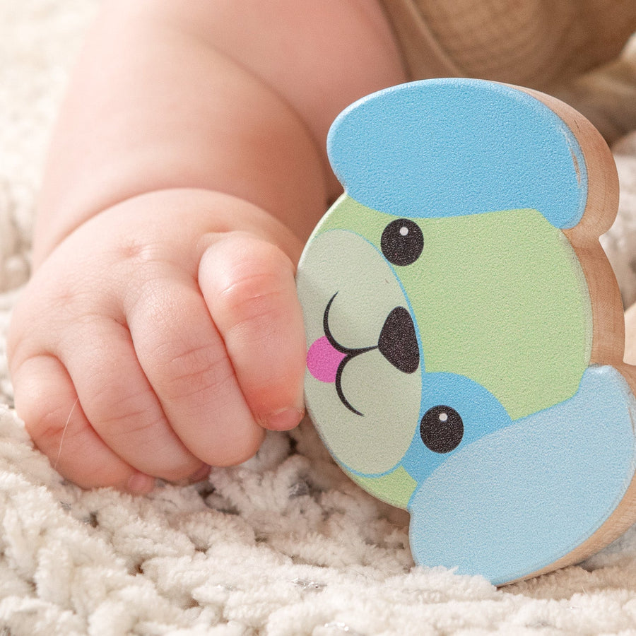 Baby holding a blue-and-green dog-shaped wooden rattle