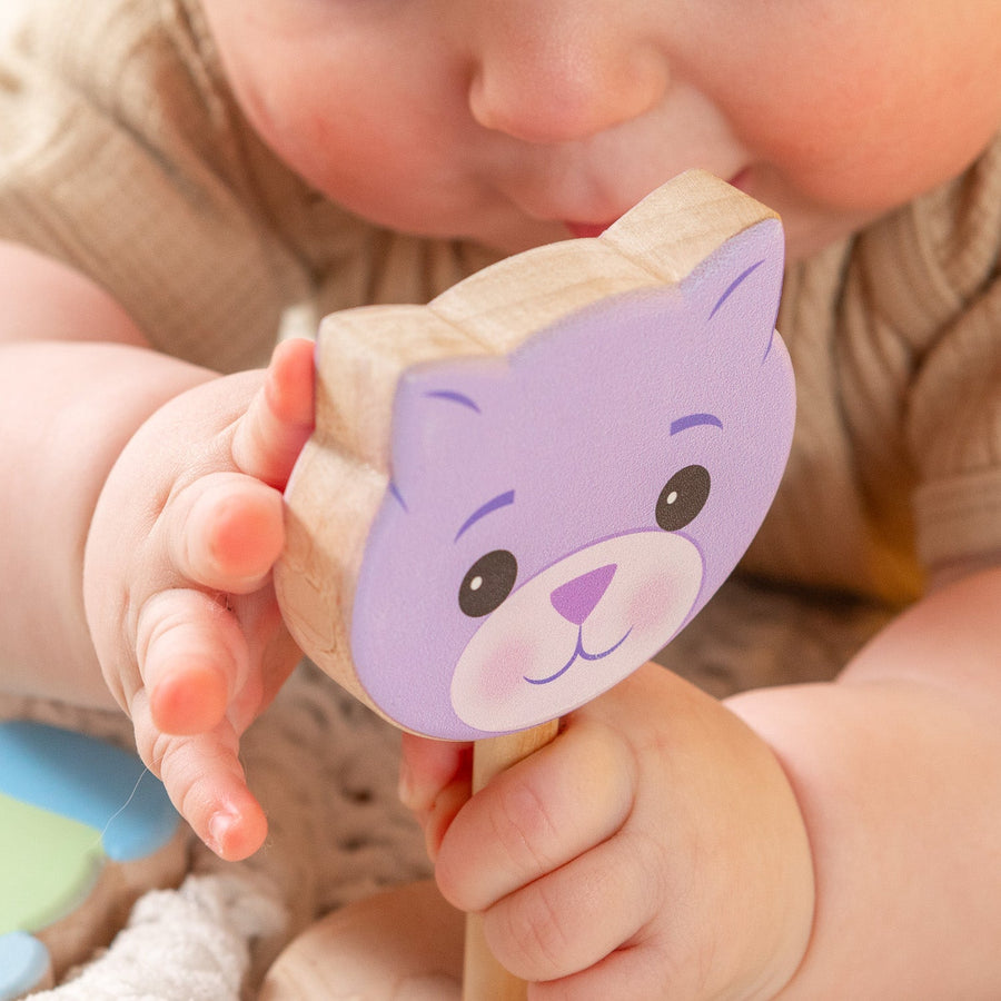 Baby holding a purple cat-shaped wooden rattle