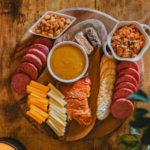 Sliced sausage, salmon, cheese, crackers, peanuts and mustard arranged for serving; board not included