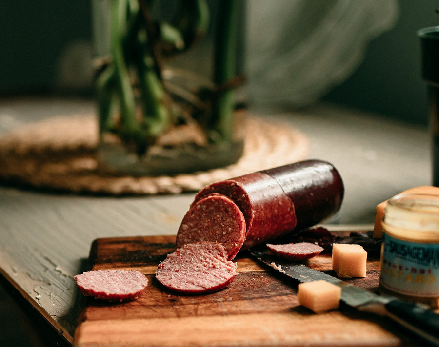 Partly sliced summer sausage beside cheese and mustard on a wooden board