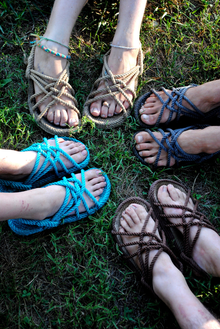 Several people wearing woven rope sandals in a circle on grass