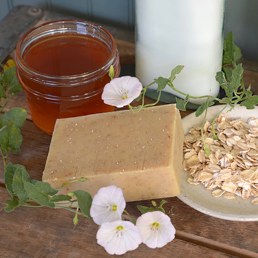 Oat and honey soap beside honey, oats, and small flowers
