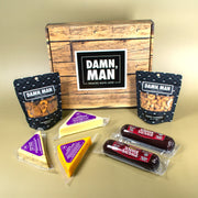 Snack box with 'Damn, Man' branding featuring cheese, sausages, and nuts on a beige background.