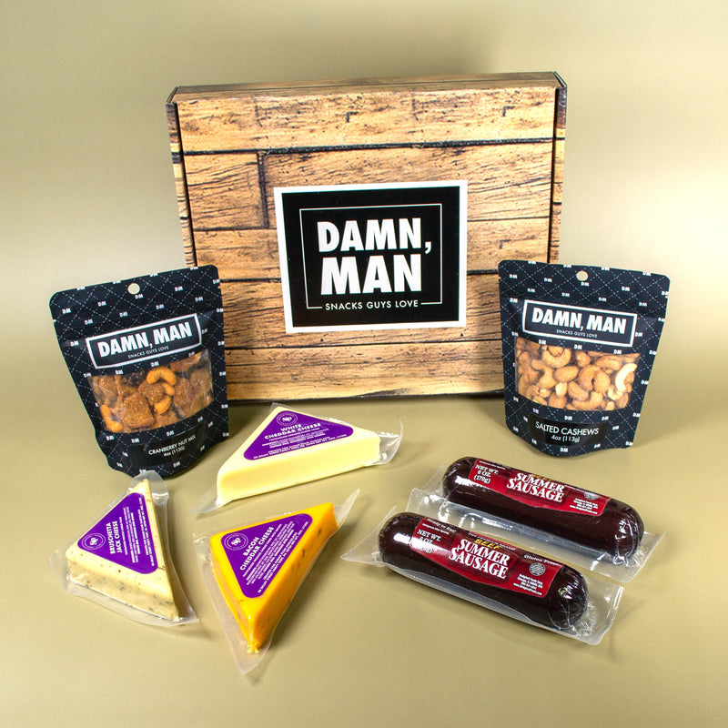 Snack box with 'Damn, Man' branding featuring cheese, sausages, and nuts on a beige background.