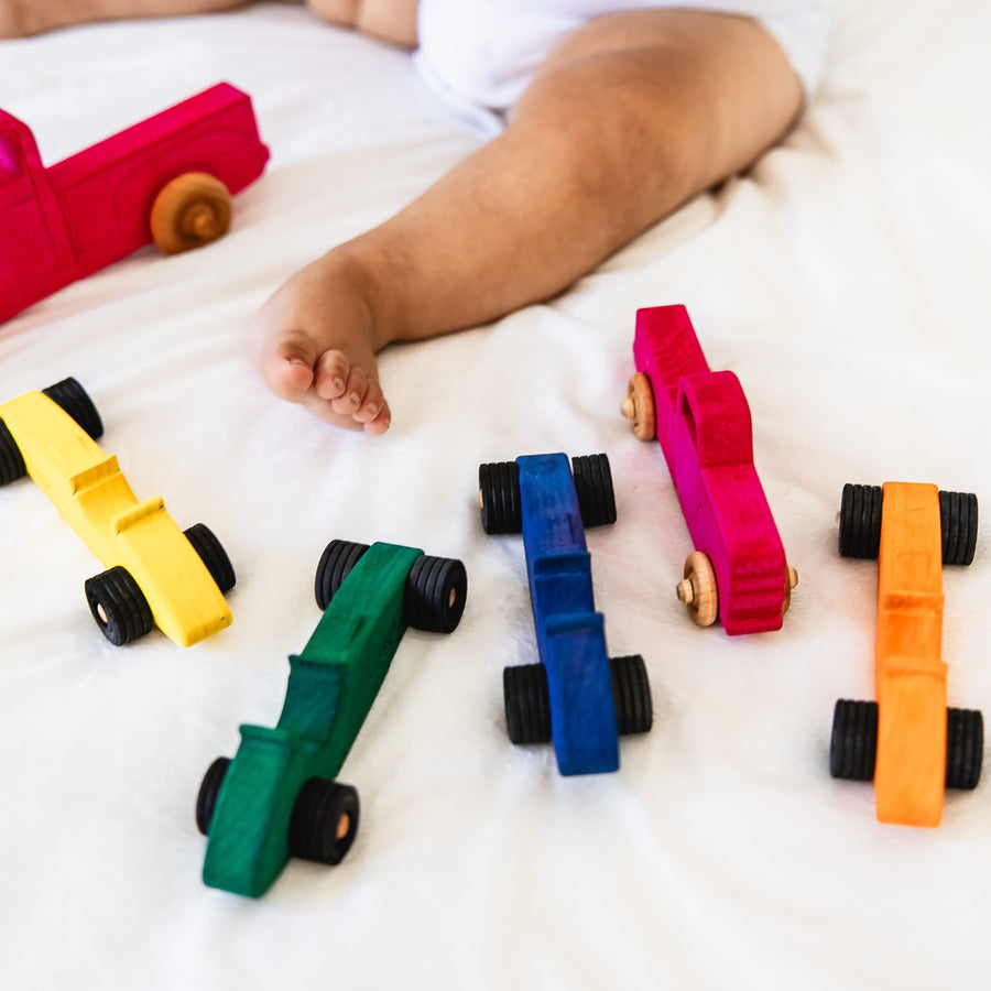 Child arranging colorful wooden toy cars and pickup trucks