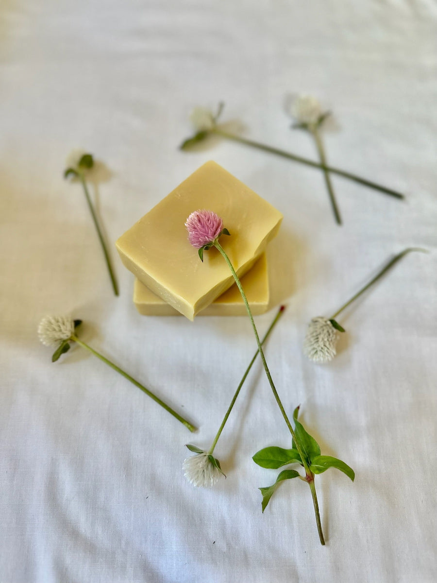 Stacked unscented soap bars with clover stems on a pale surface