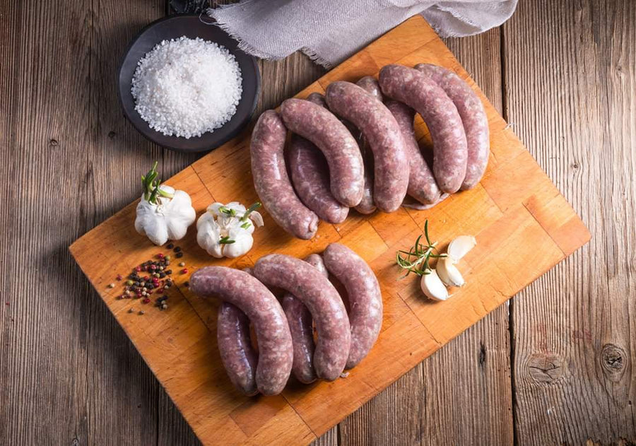 Uncooked sausage links on a cutting board with garlic and salt