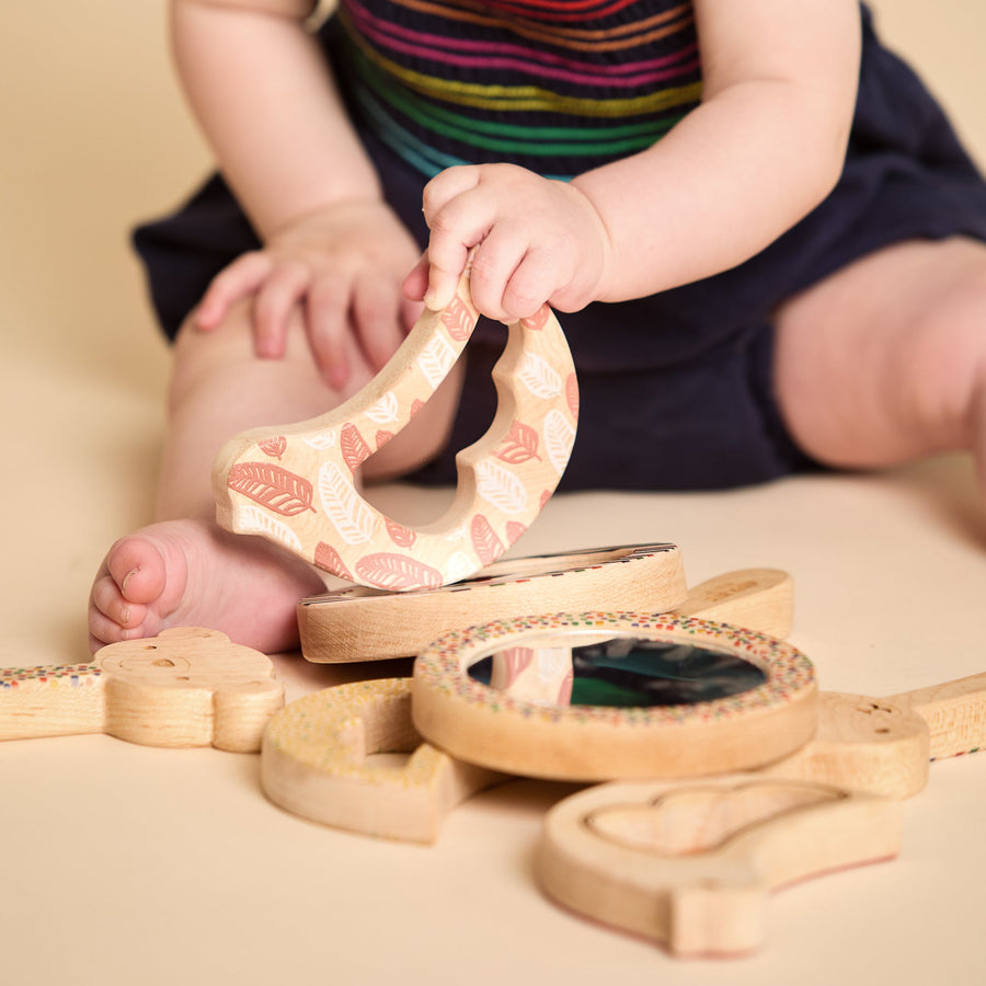Child grasping and exploring a bird-shaped wooden rattle