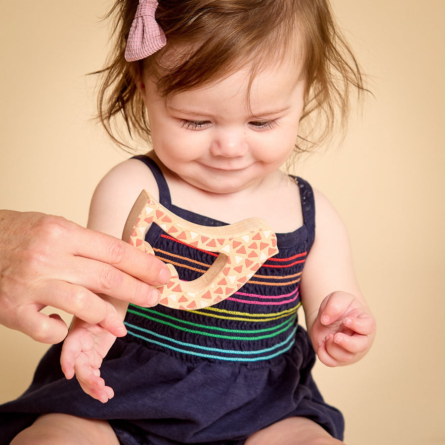 Child grasping and exploring a bird-shaped wooden rattle