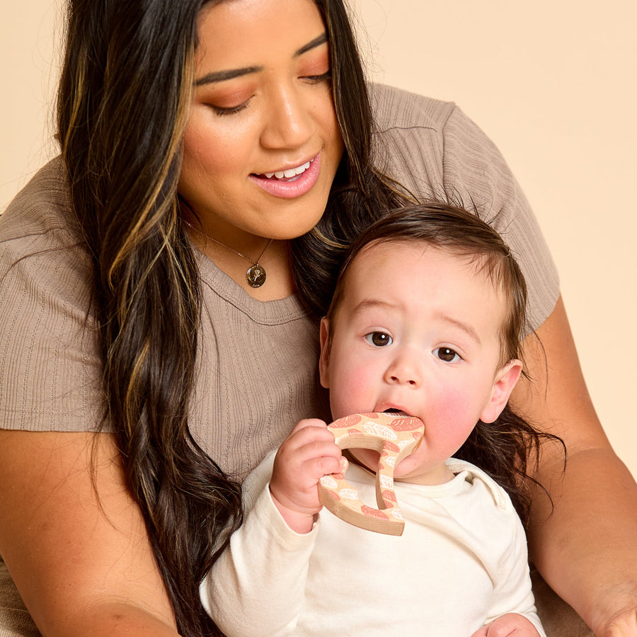 Baby holding a bird-shaped wooden rattle and teether