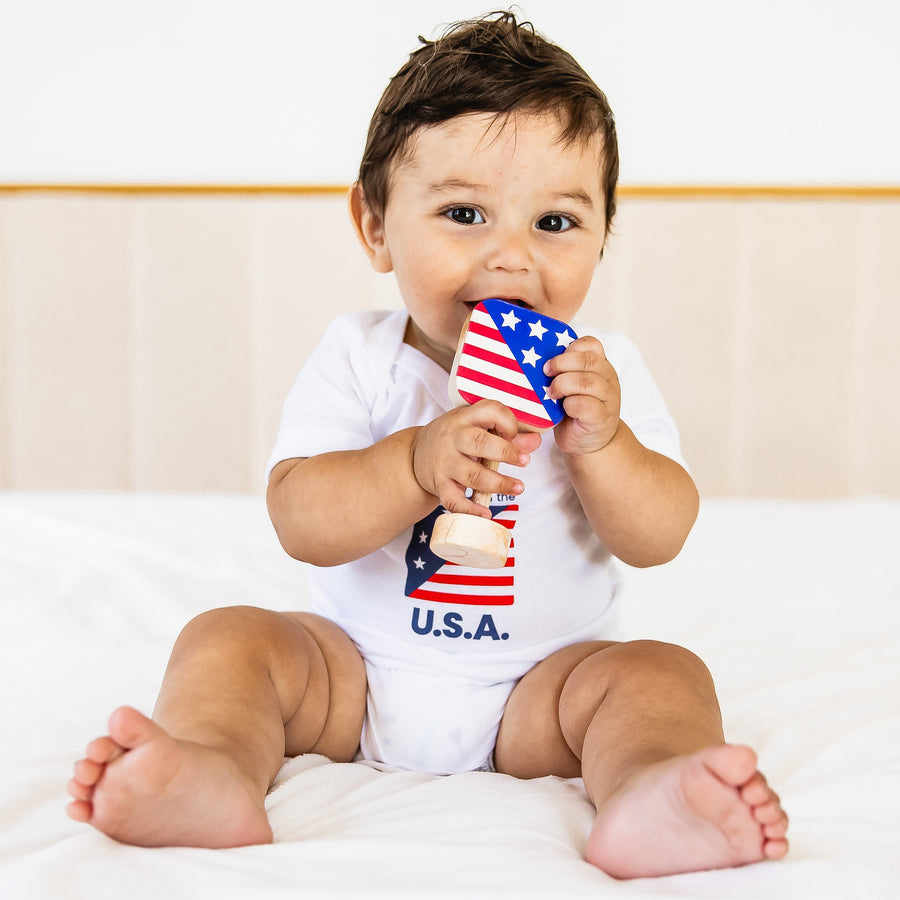 Baby holding an American flag-shaped wooden rattle