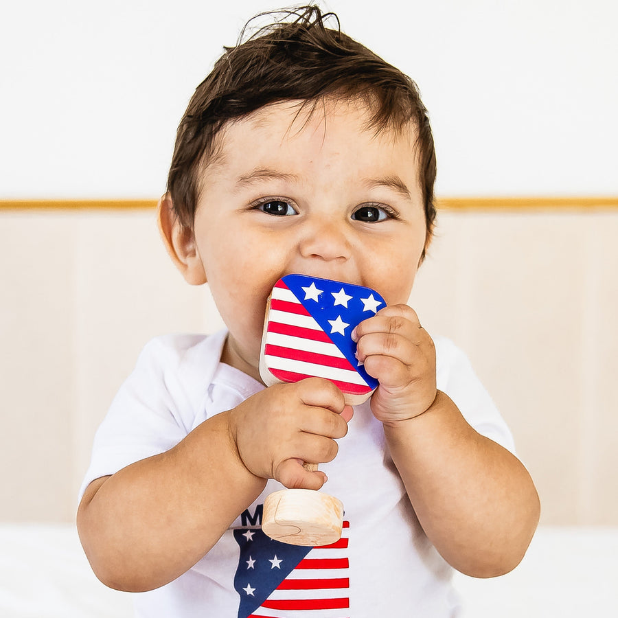 Baby holding an American flag-shaped wooden rattle