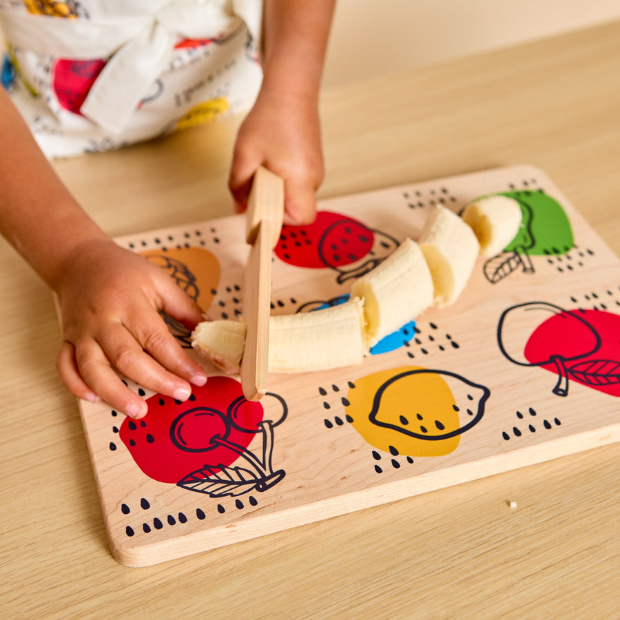 Child using a wooden knife and illustrated cutting board during food preparation