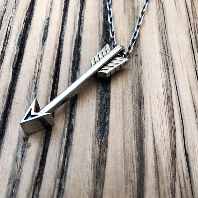 Arrow pendant and chain against weathered wood