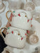 Two handmade ceramic mugs stacked together, featuring festive garland designs with red flags, gold accents, and colorful dots.