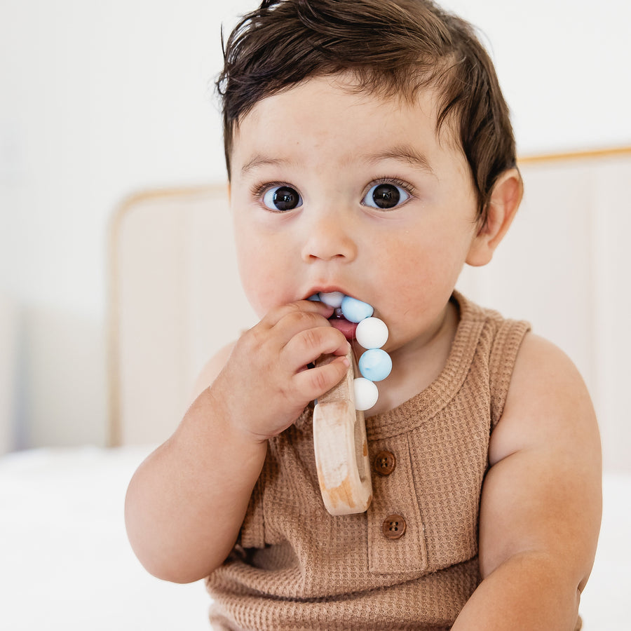 Baby holding a wooden teether with silicone beads during supervised play
