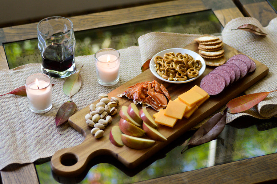 Meat, cheese, crackers and nuts on a wooden board beside wine; serving suggestion
