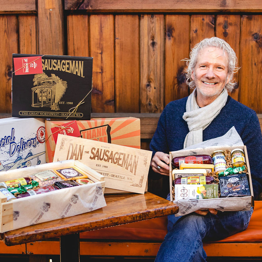 Person displaying assorted Dan The Sausageman gift boxes beside a wooden wall