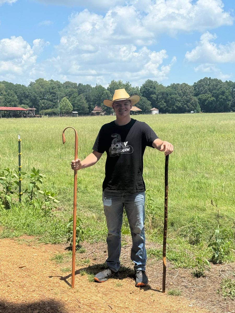 Person demonstrating two different wooden staffs outdoors