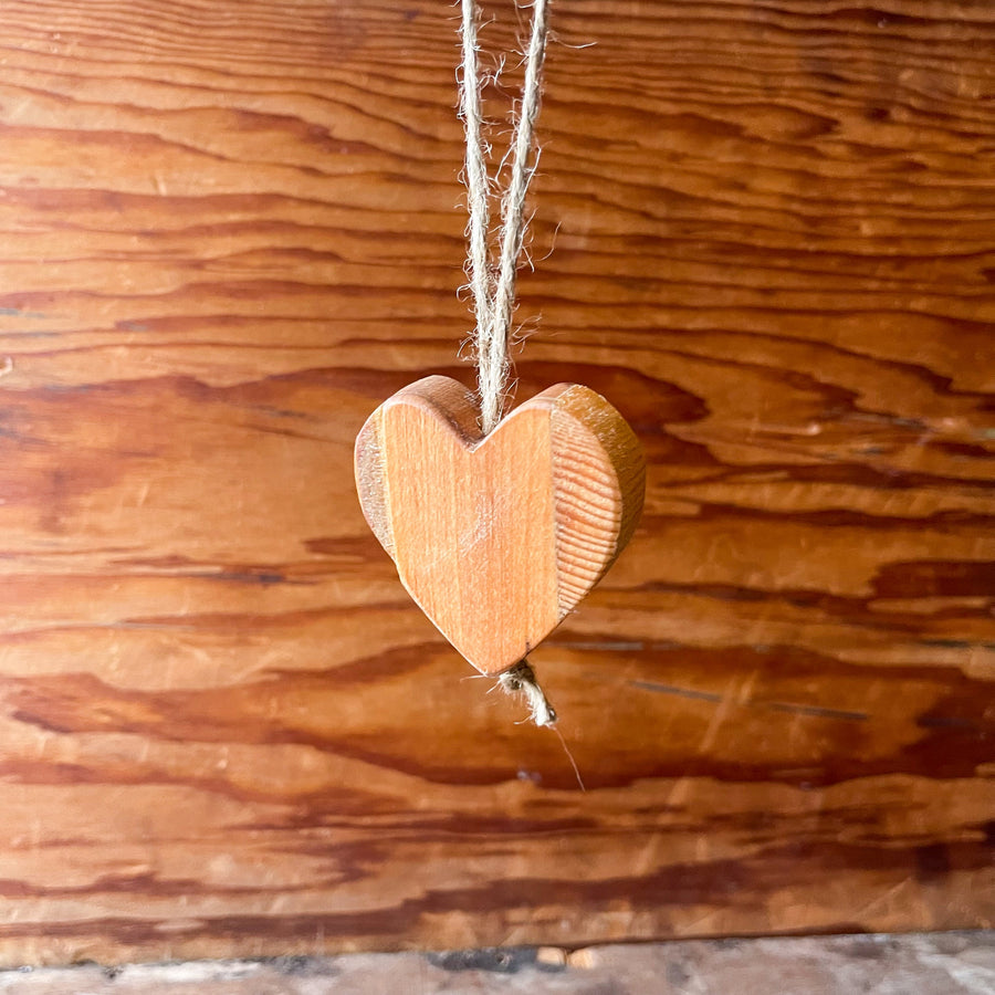 Natural wooden heart charm hanging on twine against a wood surface.