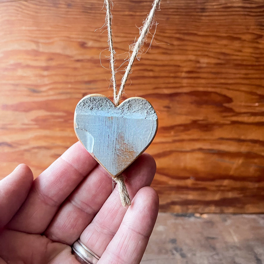 Blue wooden heart charm held against a wooden background.