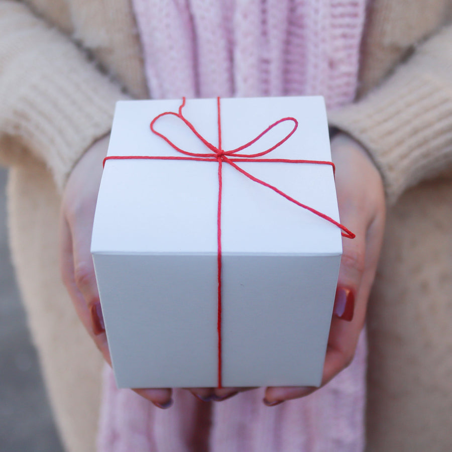 Gift box tied with red string held above printed Love Notes.