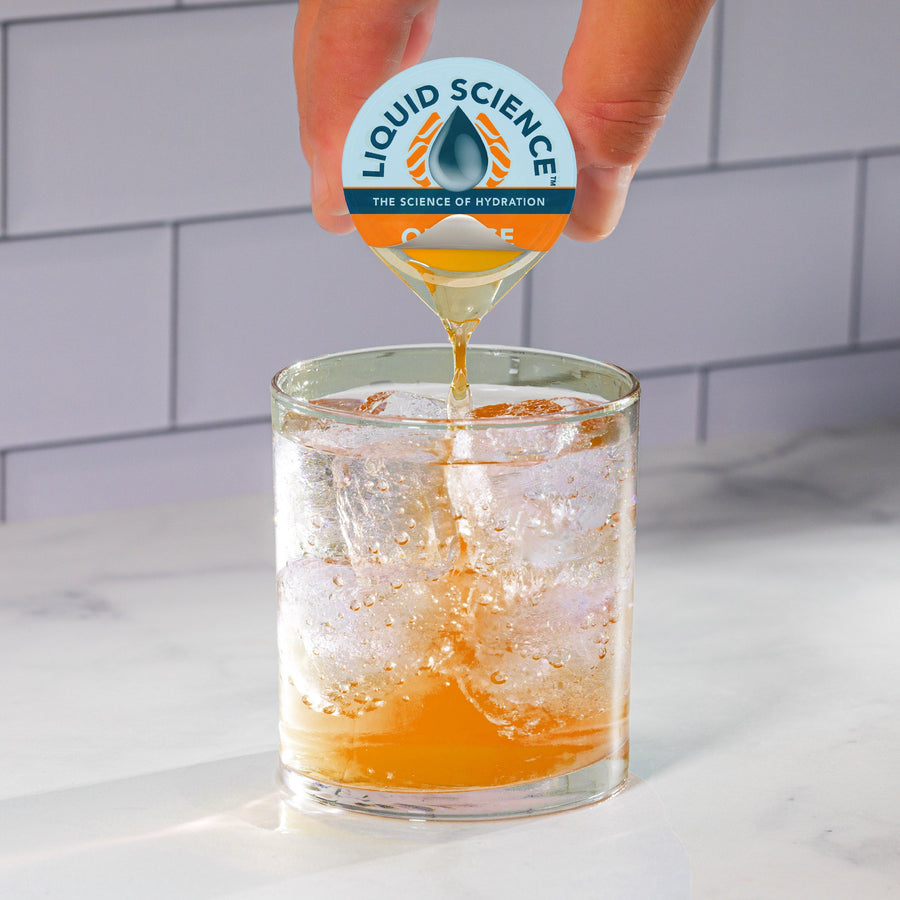Hand pouring Orange hydration concentrate into water