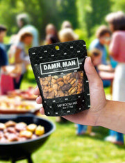 Hand holding Manly Mixed Nuts bag at outdoor barbecue event with people in the background.