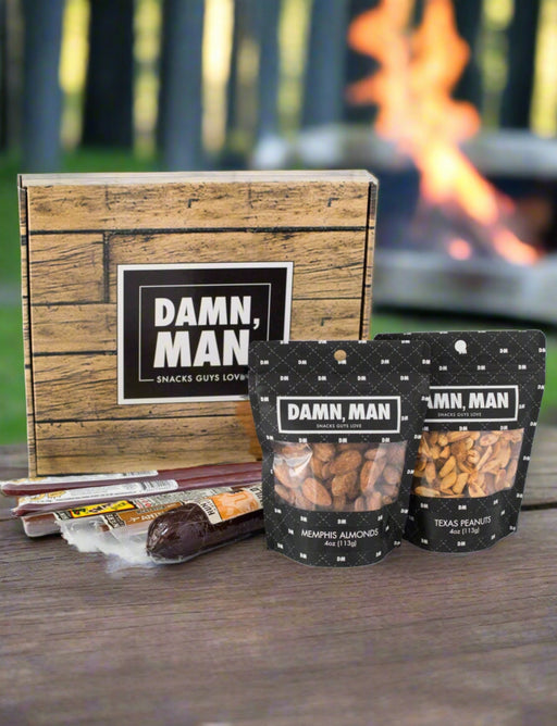 Damn Man Nuts & Exotic Meats Box with wild boar summer sausage, Memphis almonds, and Texas peanuts near a campfire