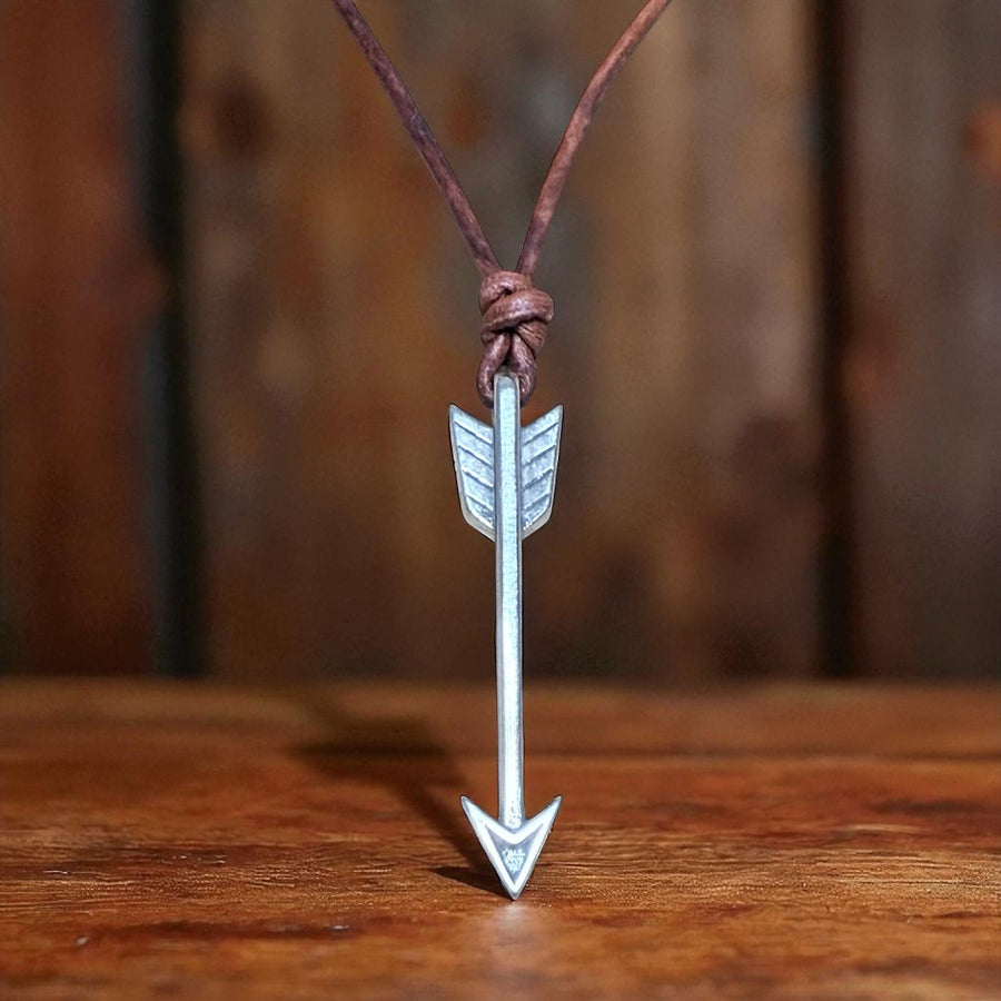 Arrow pendant on brown leather cord against wood