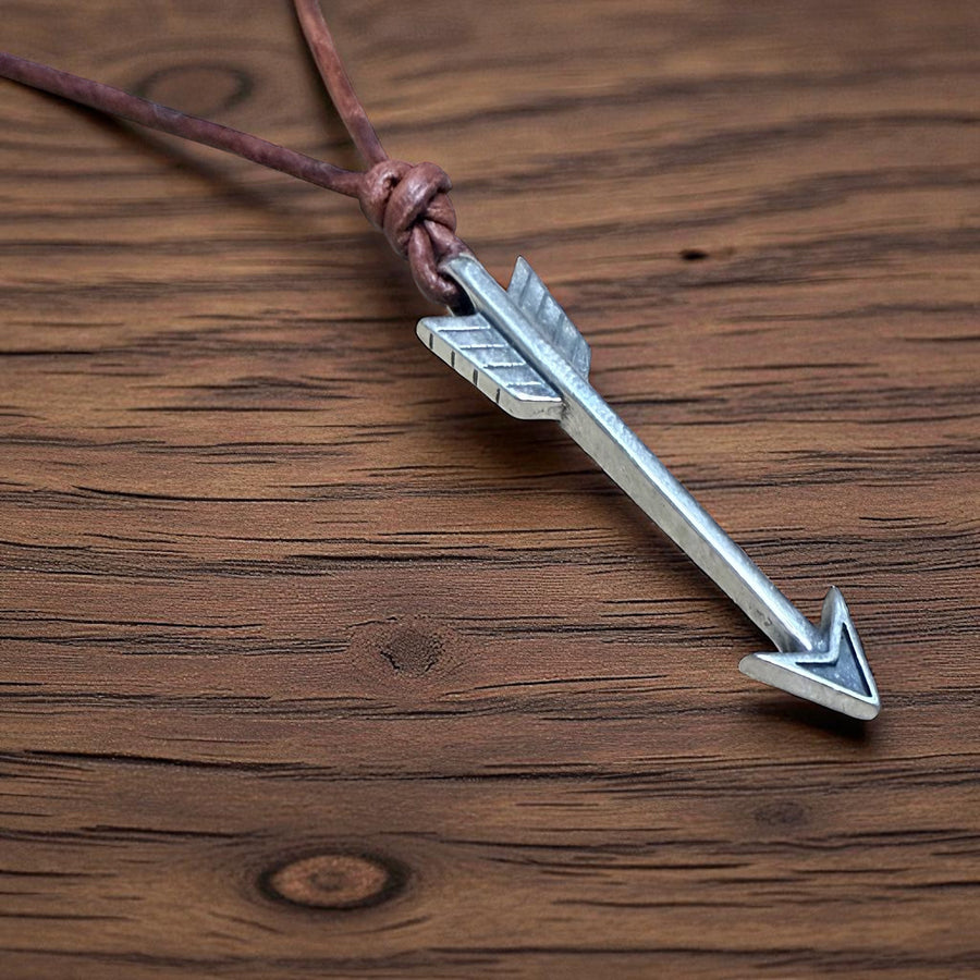 Arrow pendant and knotted brown leather cord on wood
