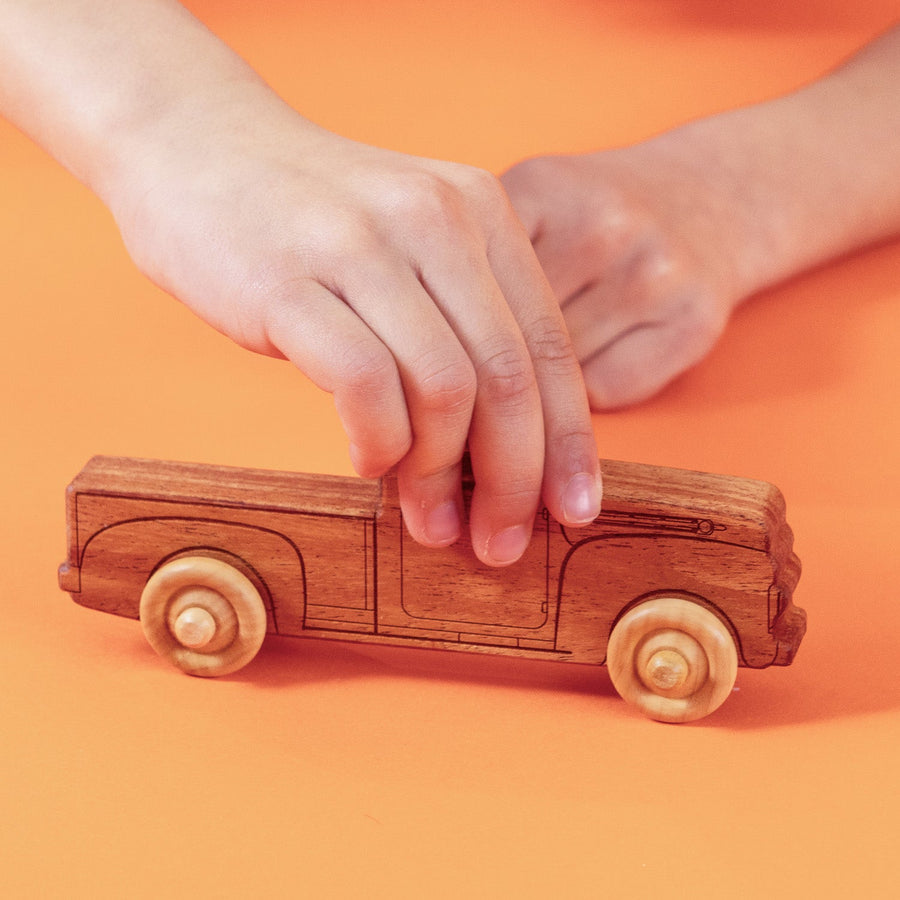 Child’s hands pushing a natural wood toy pickup truck