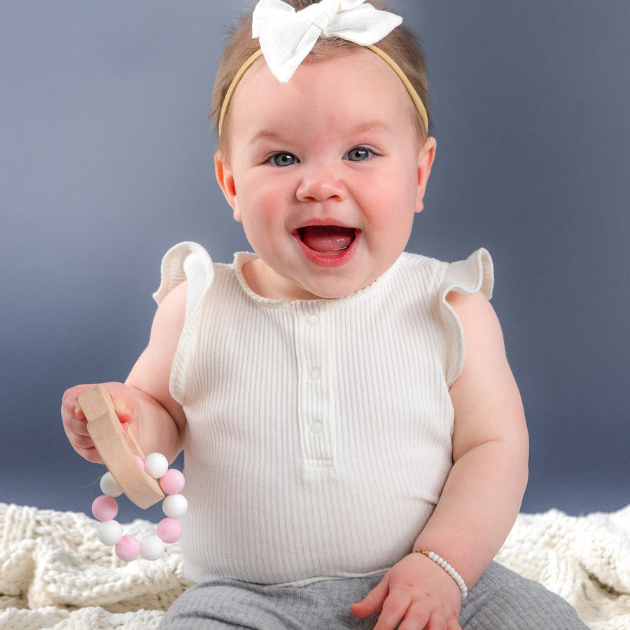 Baby holding a wooden teether with silicone beads during supervised play