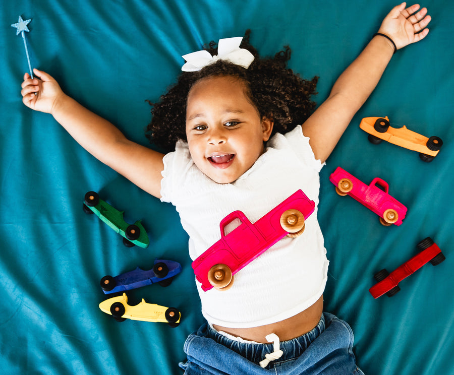 Child lying beside colorful wooden pickup trucks during play