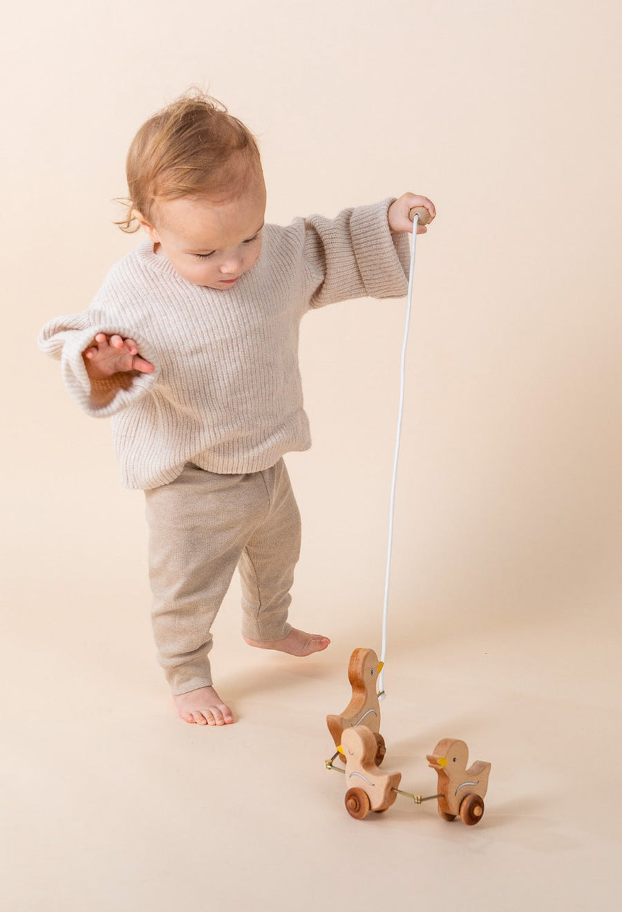 Child pulling a linked wooden animal toy across the floor