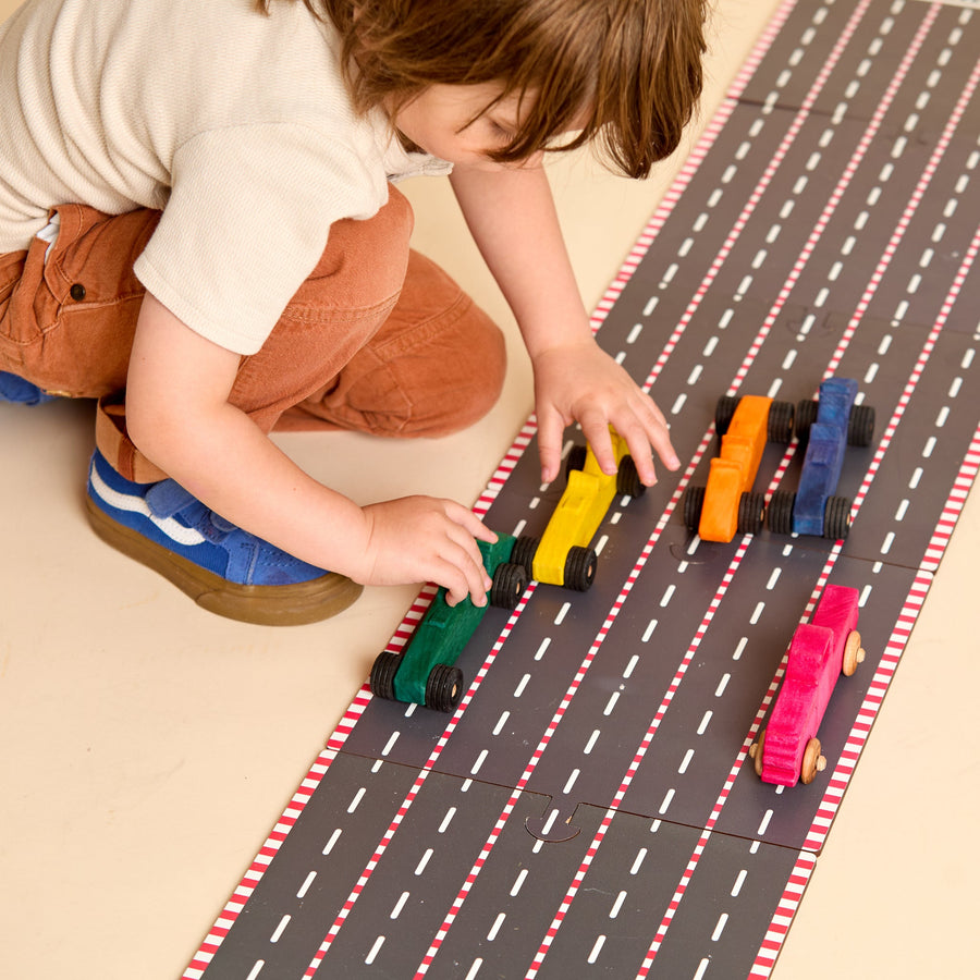 Child racing colorful wooden cars on a printed racetrack