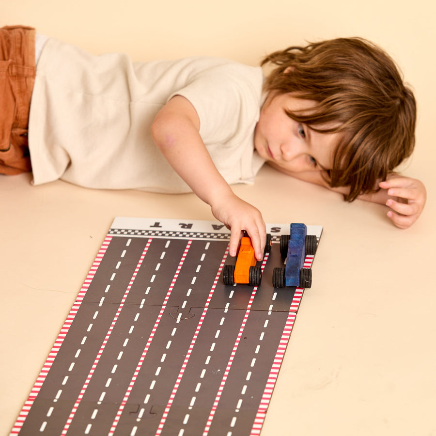Child racing colorful wooden cars on a printed racetrack