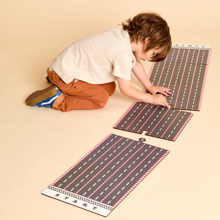 Child racing colorful wooden cars on a printed racetrack