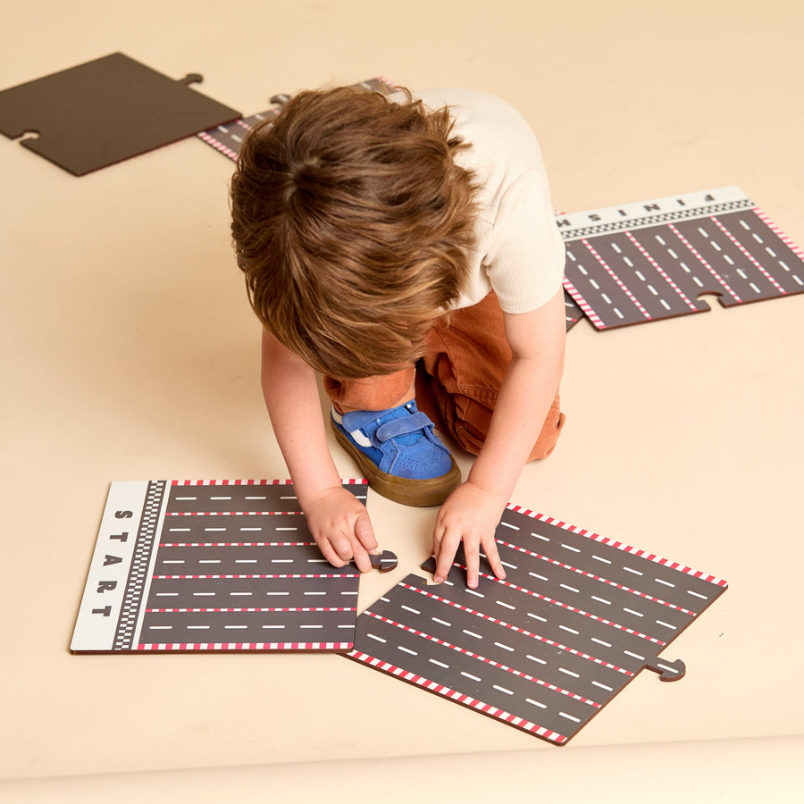 Child racing colorful wooden cars on a printed racetrack