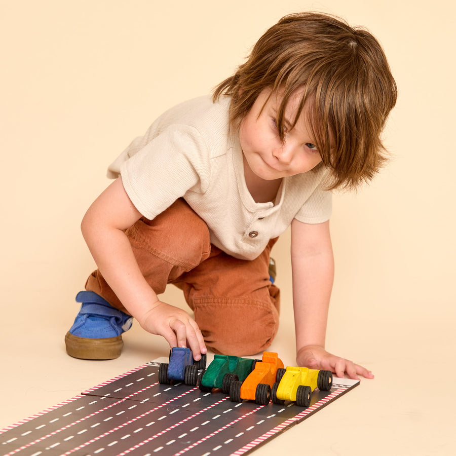 Child racing colorful wooden cars on a printed racetrack
